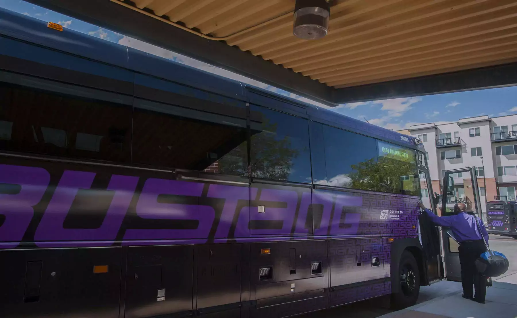 Purple and black Bustang bus at stop with driver