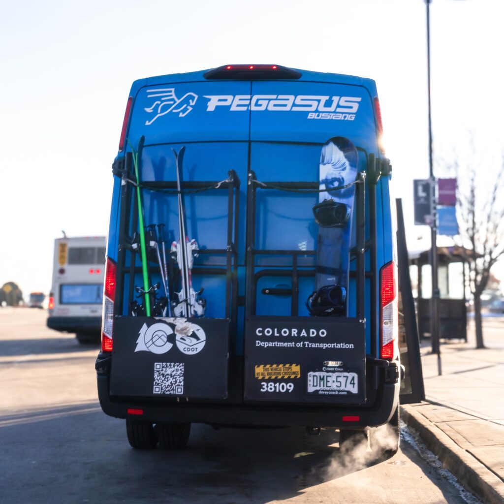 Photo of the back of the Pegasus blue van with skis and snowboard in the rack
